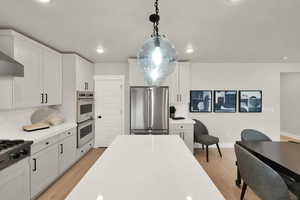 Kitchen with appliances with stainless steel finishes, light wood finished floors, backsplash, light countertops, and recessed lighting