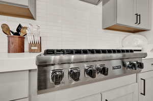 Kitchen view of decorative backsplash, stainless steel gas stovetop, and light countertops