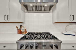 Kitchen featuring wall chimney range hood, light countertops, backsplash, and stainless steel gas stovetop
