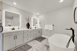 Full bath featuring double vanity, a soaking tub, marble look tiles, recessed lighting, and baseboards