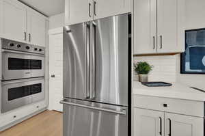 Kitchen with appliances with stainless steel finishes, tasteful backsplash, light countertops, light wood-style flooring, and white cabinetry