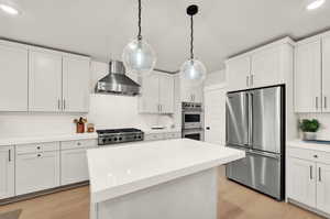 Kitchen featuring appliances with stainless steel finishes, wall chimney range hood, backsplash, light wood finished floors, and light countertops