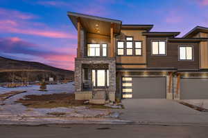 Contemporary home featuring a balcony, a mountain view, stone siding, an attached garage, and driveway