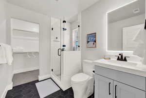 Bathroom with a spacious closet, vanity, a shower stall, toilet, and tile patterned flooring