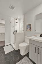 Full bathroom with vanity, a shower stall, toilet, tile patterned flooring, and a walk in closet