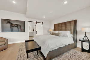 Bedroom featuring a barn door, baseboards, wood finished floors, recessed lighting, and ensuite bathroom