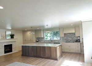 Kitchen with light wood-style floors, a center island, tasteful backsplash, a fireplace, and custom exhaust hood