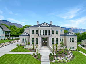 View of front of property featuring stone siding, a balcony, a chimney, a mountain view, and a front yard