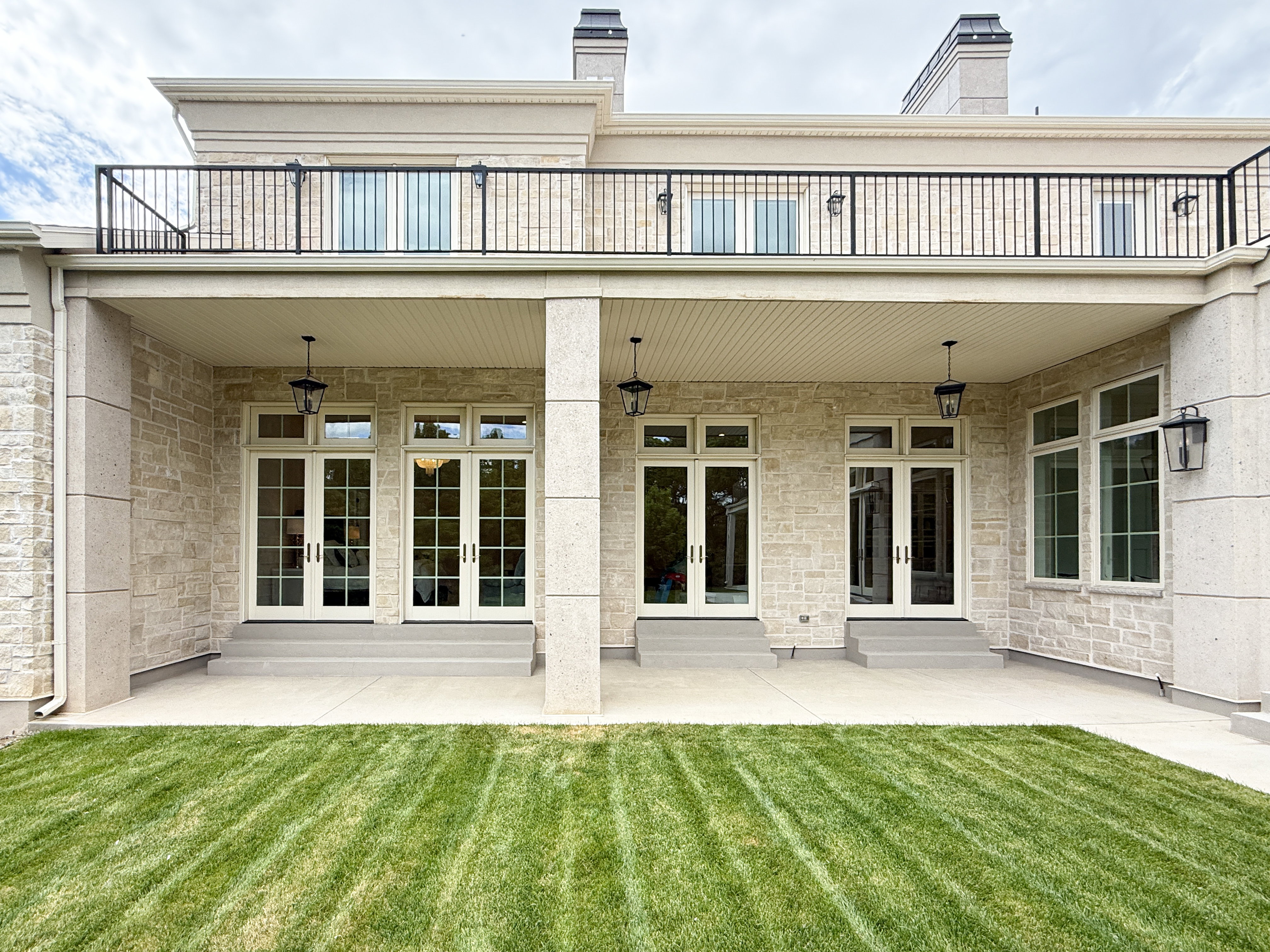 Rear view of house featuring french doors, a balcony, a yard, and stone siding