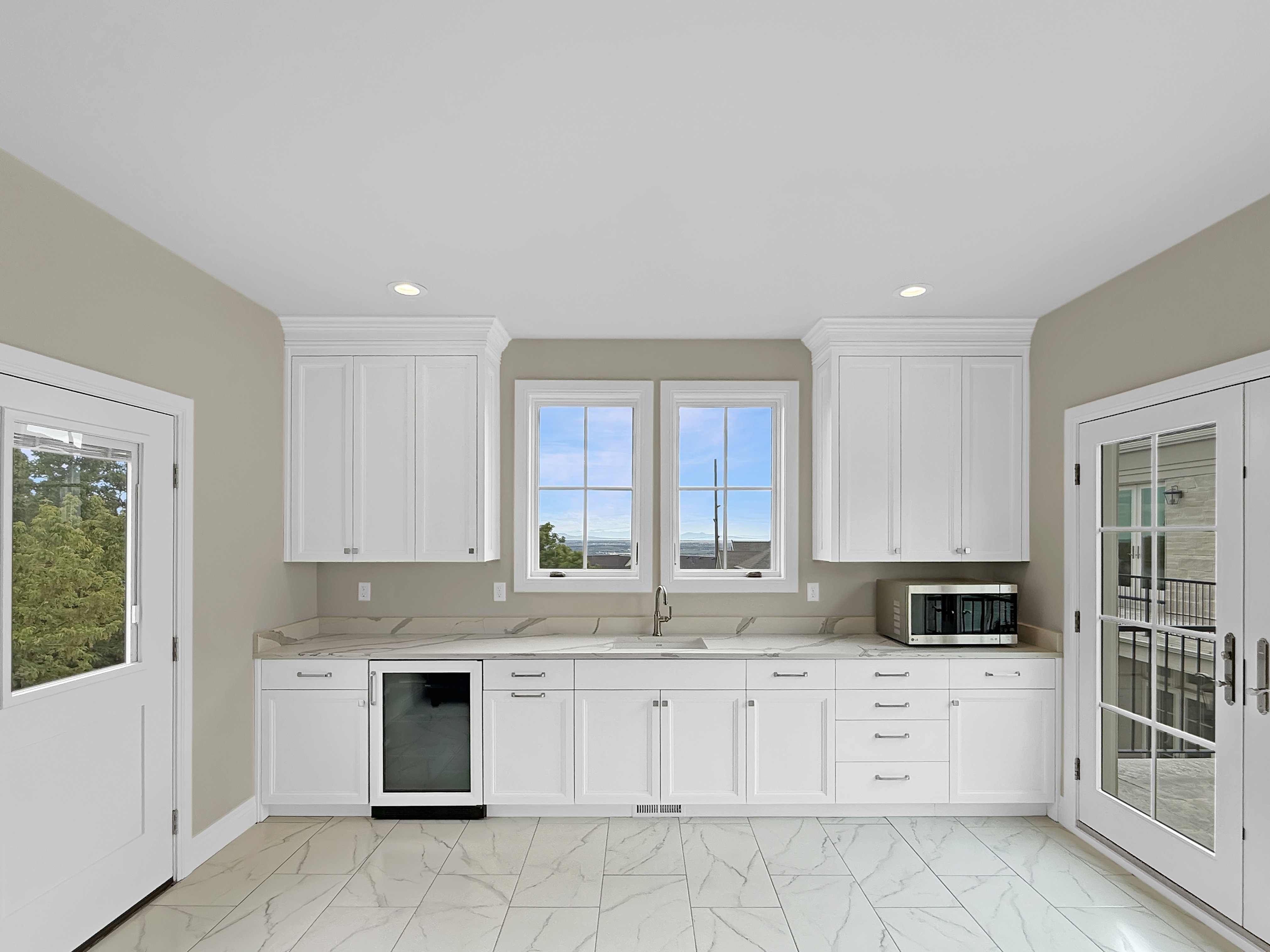 Above garage kitchen with beverage cooler, stainless steel microwave, light marble finish flooring, a sink, and plenty of natural light