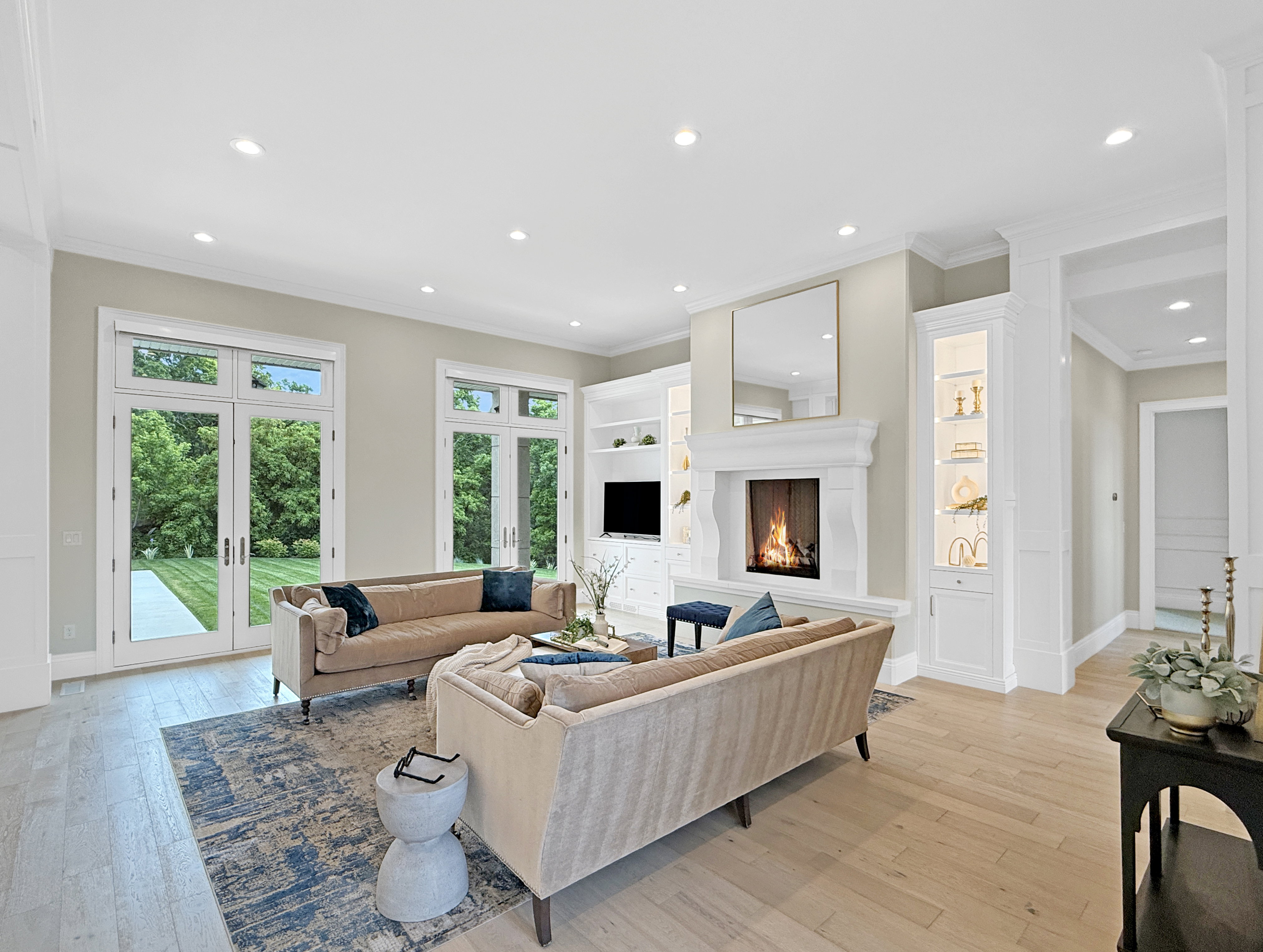 Living room featuring french doors, light wood-style floors, crown molding, a warm lit fireplace, and recessed lighting