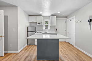 Kitchen with light countertops, a center island, a textured ceiling, baseboards, and white appliances