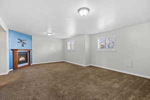 Unfurnished living room with carpet flooring, a glass covered fireplace, baseboards, and a textured ceiling