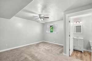 Unfurnished bedroom featuring baseboards, a textured ceiling, light colored carpet, ensuite bathroom, and a sink