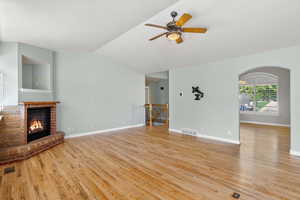 Unfurnished living room featuring light wood finished floors, a brick fireplace, a ceiling fan, lofted ceiling, and baseboards