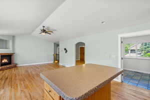 Kitchen featuring arched walkways, a ceiling fan, a brick fireplace, a center island, and lofted ceiling