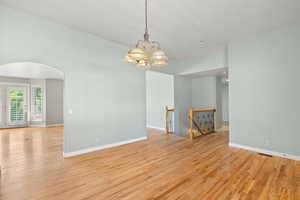 Empty room featuring arched walkways, light wood finished floors, a chandelier, and baseboards