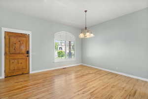 Empty room featuring light wood finished floors, baseboards, and a chandelier
