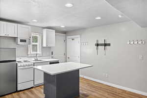 Kitchen featuring white appliances, a sink, light countertops, a kitchen island, and a textured ceiling