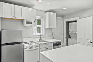 Kitchen with stainless steel appliances, stacked washer / dryer, a sink, white cabinetry, and recessed lighting