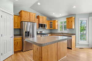 Kitchen featuring appliances with stainless steel finishes, lofted ceiling, light wood-style floors, a sink, and a kitchen island