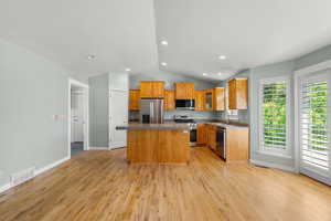 Kitchen featuring appliances with stainless steel finishes, a sink, a center island, lofted ceiling, and light wood-style flooring