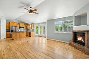 Kitchen featuring appliances with stainless steel finishes, a kitchen island, light wood-style flooring, open floor plan, and lofted ceiling