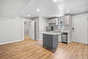 Kitchen with stainless steel appliances, light wood-type flooring, a sink, light countertops, and baseboards