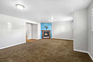 Unfurnished living room featuring a warm lit fireplace, carpet, and baseboards