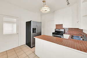 Kitchen with stainless steel appliances, white cabinets, tile countertops, backsplash, and light tile patterned flooring