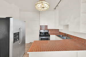 Kitchen featuring stainless steel appliances, a sink, light tile patterned flooring, and white cabinets