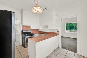 Kitchen featuring stainless steel appliances, a sink, white cabinetry, light tile patterned floors, and a peninsula