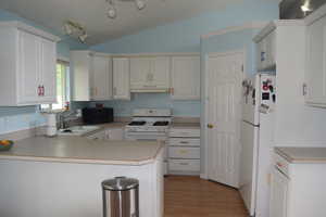 Kitchen with white appliances, under cabinet range hood, a sink, a peninsula, and vaulted ceiling