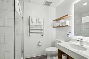 Full bath with radiator, toilet, vanity, wood finished floors, and a tile shower
