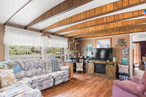 Living area with beam ceiling, wood finished floors, and a glass covered fireplace