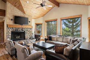 Living room featuring wood-type flooring, ceiling fan, a fireplace, wooden ceiling with exposed beams, and high vaulted ceiling
