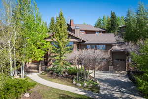 View of front of home with driveway, a chimney, stairway, and stone siding