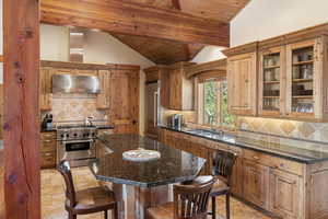 Kitchen with under cabinet range hood, high end appliances, a sink, a kitchen breakfast bar, and wooden ceiling
