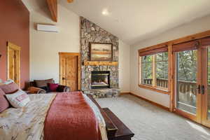 Carpeted bedroom with a wall unit AC, a stone fireplace, access to outside, baseboards, and high vaulted ceiling