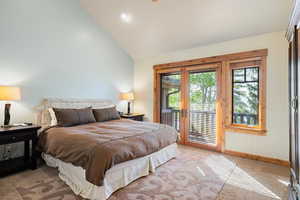 Bedroom with access to outside, multiple windows, light colored carpet, baseboards, and high vaulted ceiling