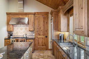 Kitchen featuring under cabinet range hood, a sink, backsplash, wood ceiling, and brown cabinetry