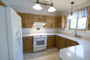 Kitchen with white appliances, a sink, under cabinet range hood, backsplash, and brown cabinets