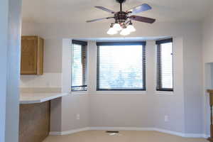 Unfurnished dining area with ceiling fan, baseboards, and light carpet