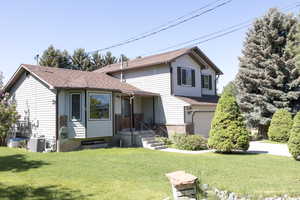View of front facade with a garage, a front yard, roof with shingles, and cooling unit