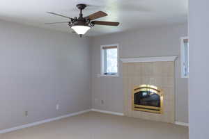 Unfurnished living room with carpet flooring, a tile fireplace, a ceiling fan, and heating unit