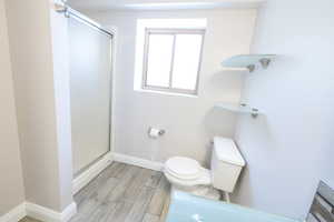 Full bathroom with a stall shower, toilet, wood finished floors, and baseboards