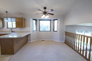 Kitchen featuring brown cabinetry, light countertops, light colored carpet, ceiling fan, and a peninsula