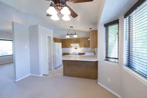 Kitchen with white appliances, under cabinet range hood, light countertops, brown cabinets, and light carpet
