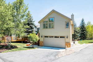 View of front facade featuring a chimney, asphalt driveway, an attached garage, stone siding, and central AC unit