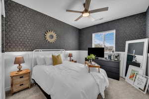 Bedroom with wainscoting, wallpapered walls, light carpet, and ceiling fan